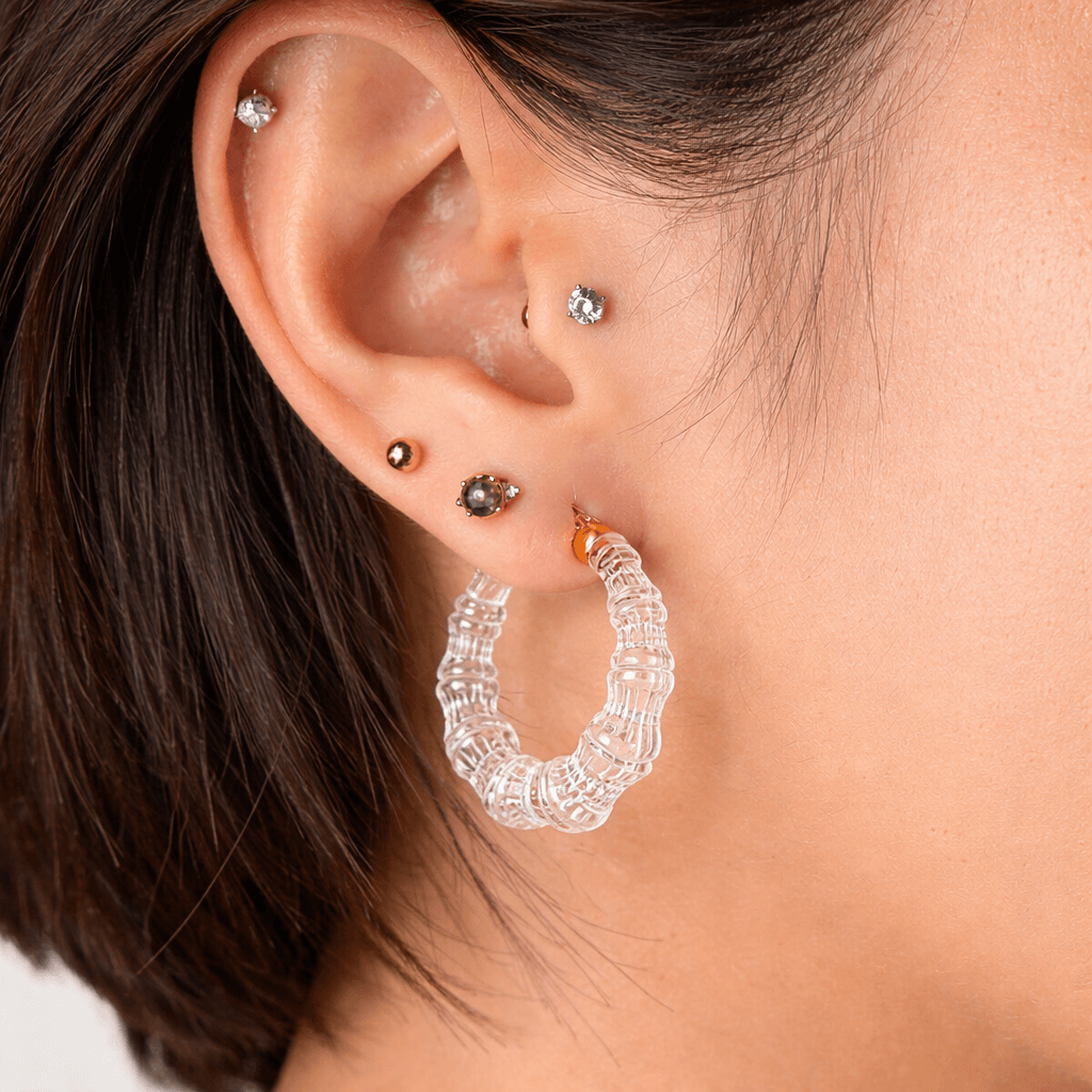 Close-up of an ear with multiple earrings including a clear bamboo hoop earring.