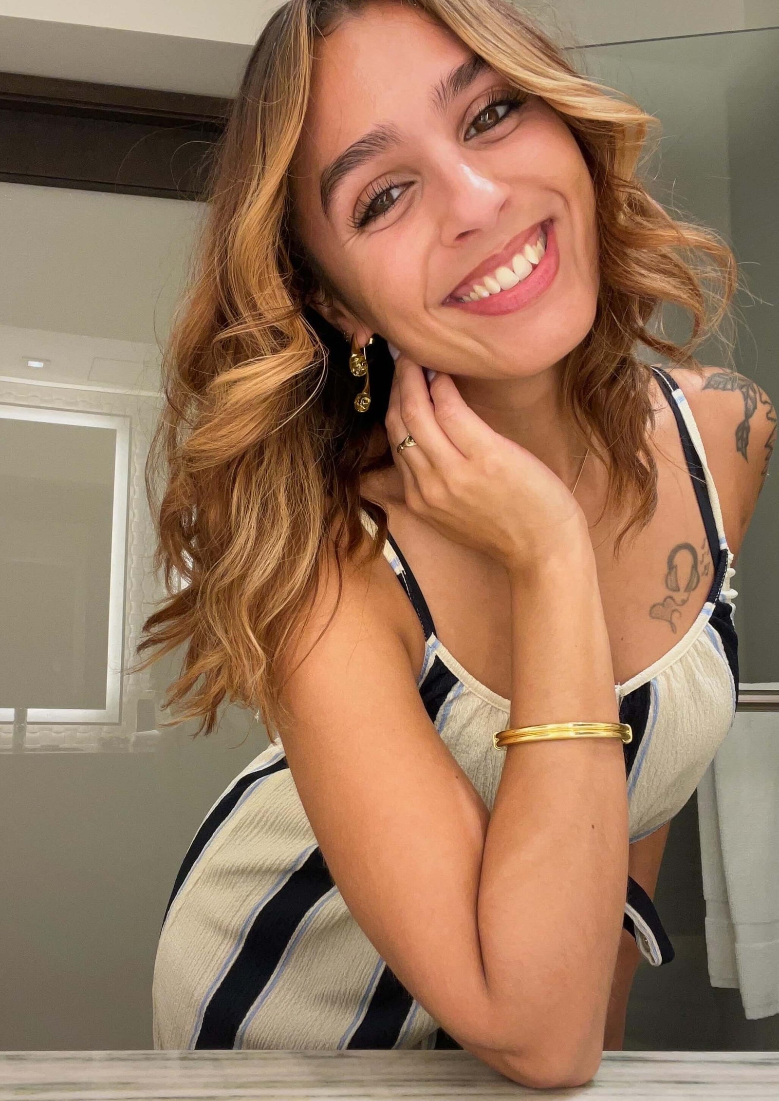 Woman with styled hair and makeup, wearing a striped top, indoors.