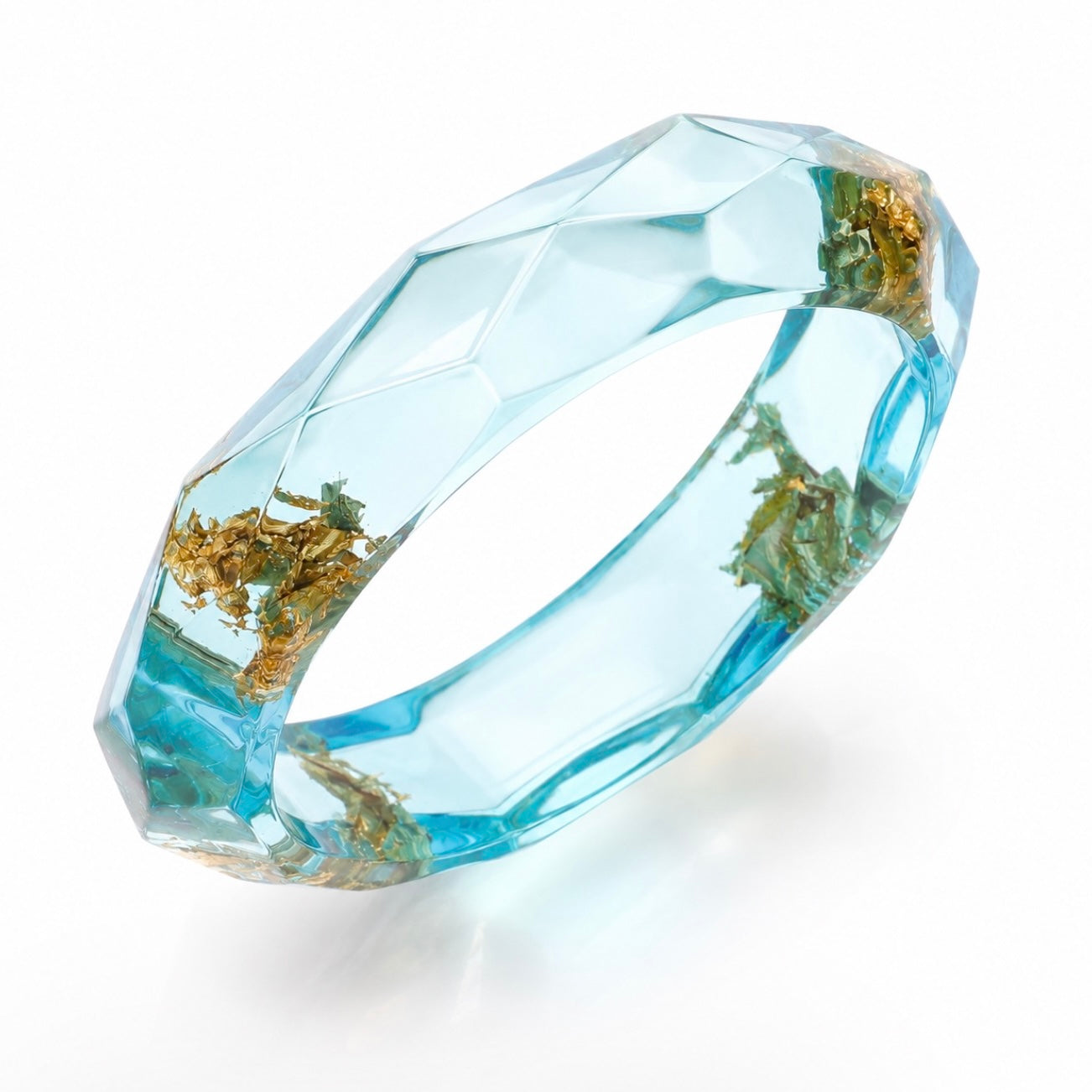 A faceted clear resin ring with light blue liquid-filled facets and embedded gold leaf elements, shown on a white background.