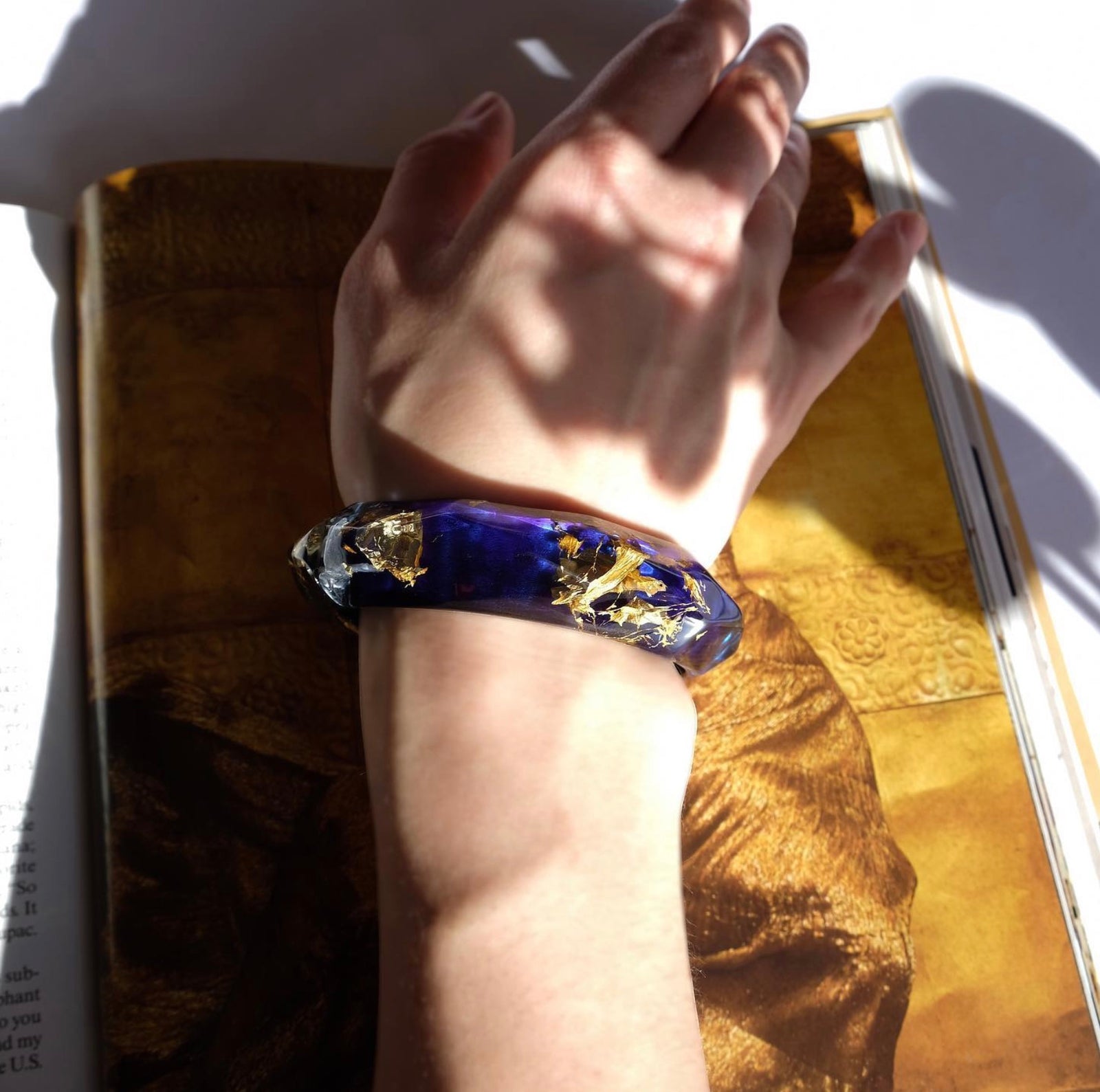 Hand wearing a blue and gold bracelet on a book