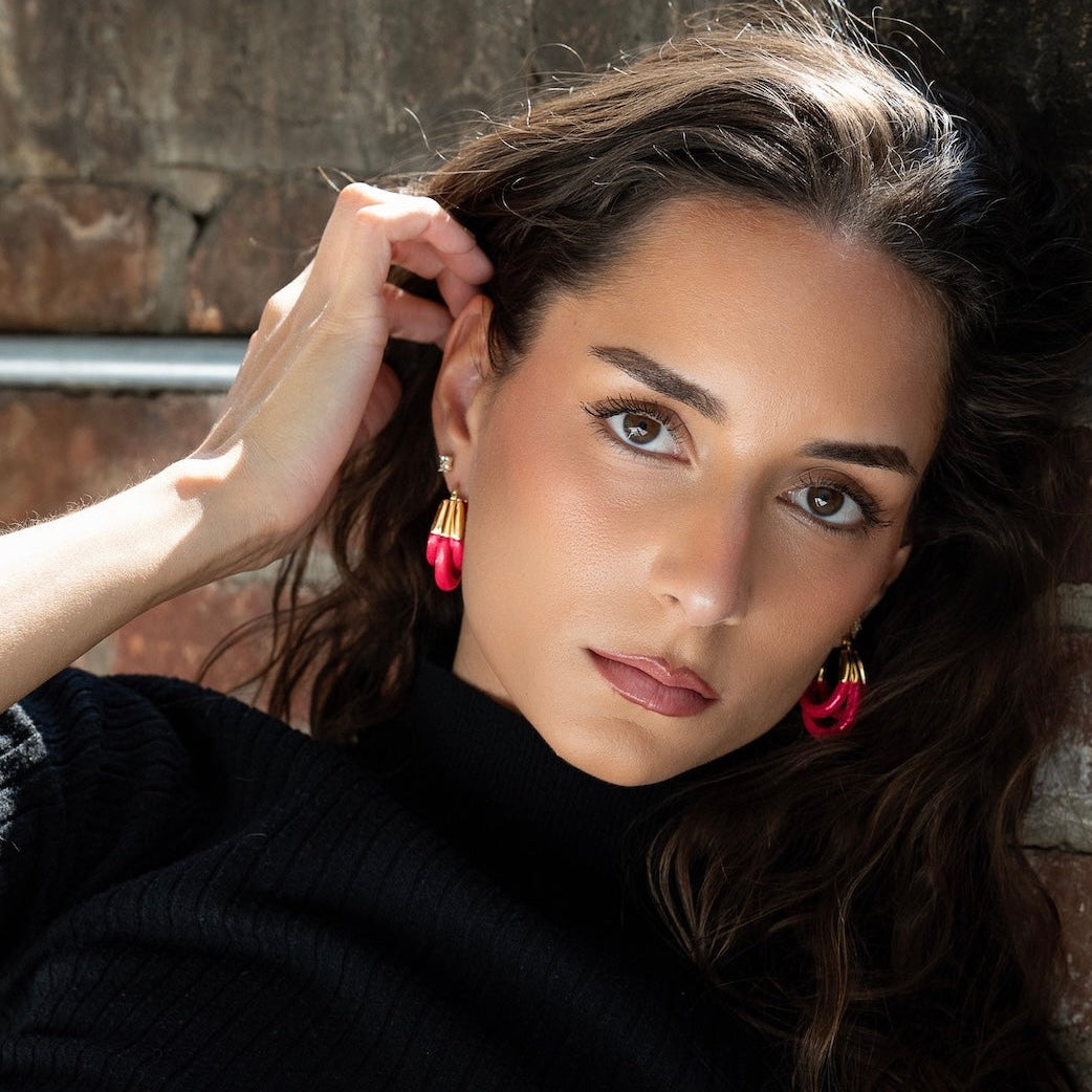 Woman with dark hair and pink triple hoop earrings against a brick wall