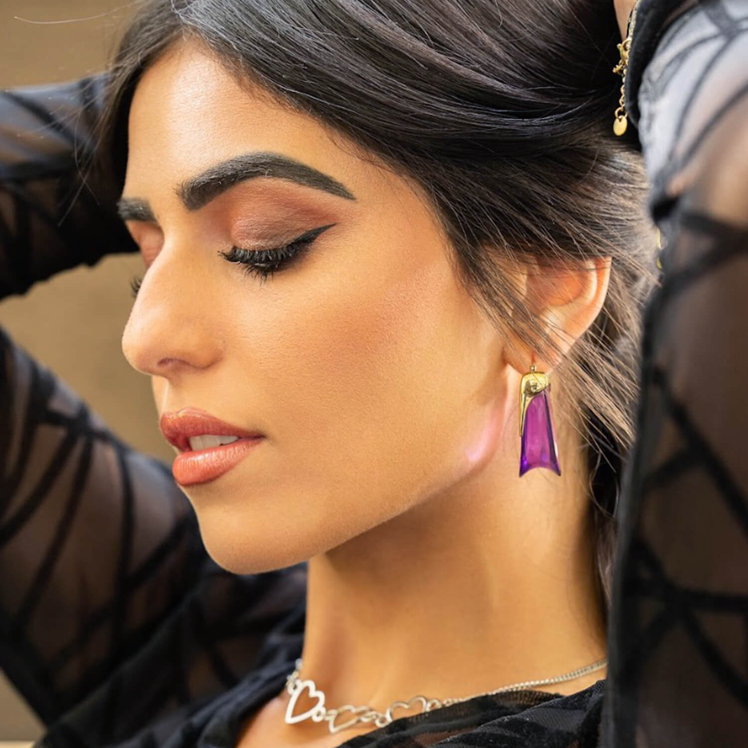 Close-up of a woman wearing a purple teardrop earring with a blurred background