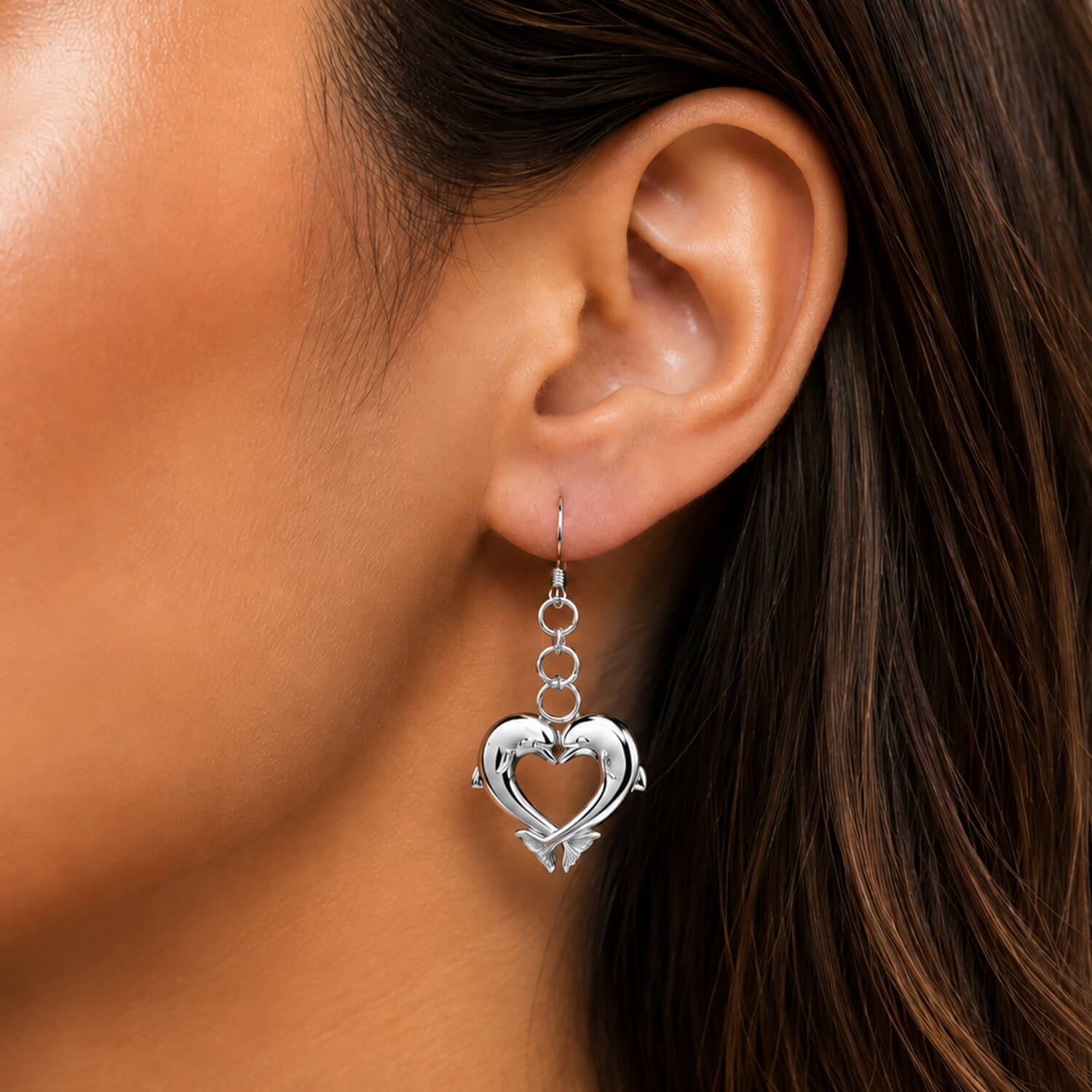Silver heart-shaped dolphin earring worn by a person with dark hair.