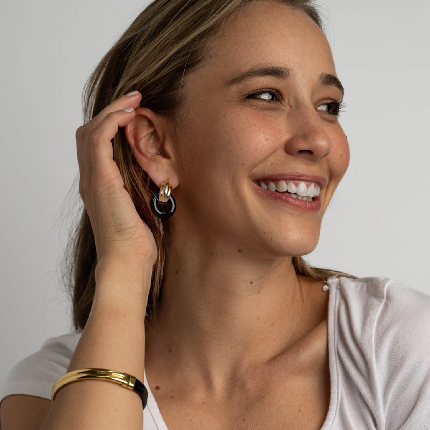 Woman wearing gold hoop earrings and a gold bracelet, smiling.