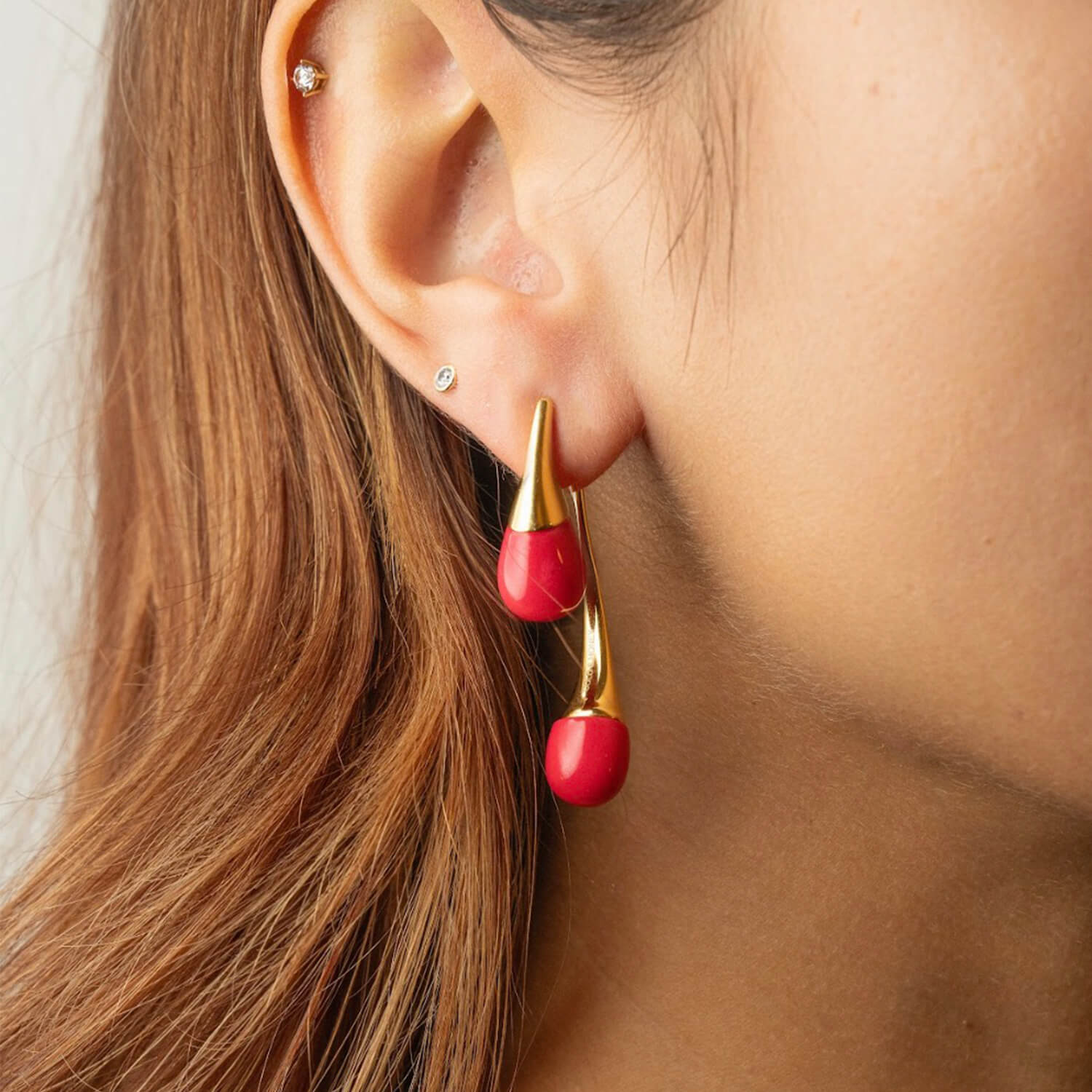 Close-up of an ear wearing a red and gold earring with a blurred background