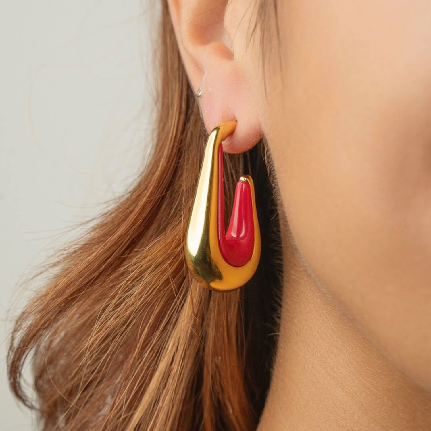 Gold and pink earring worn by a person with brown hair.