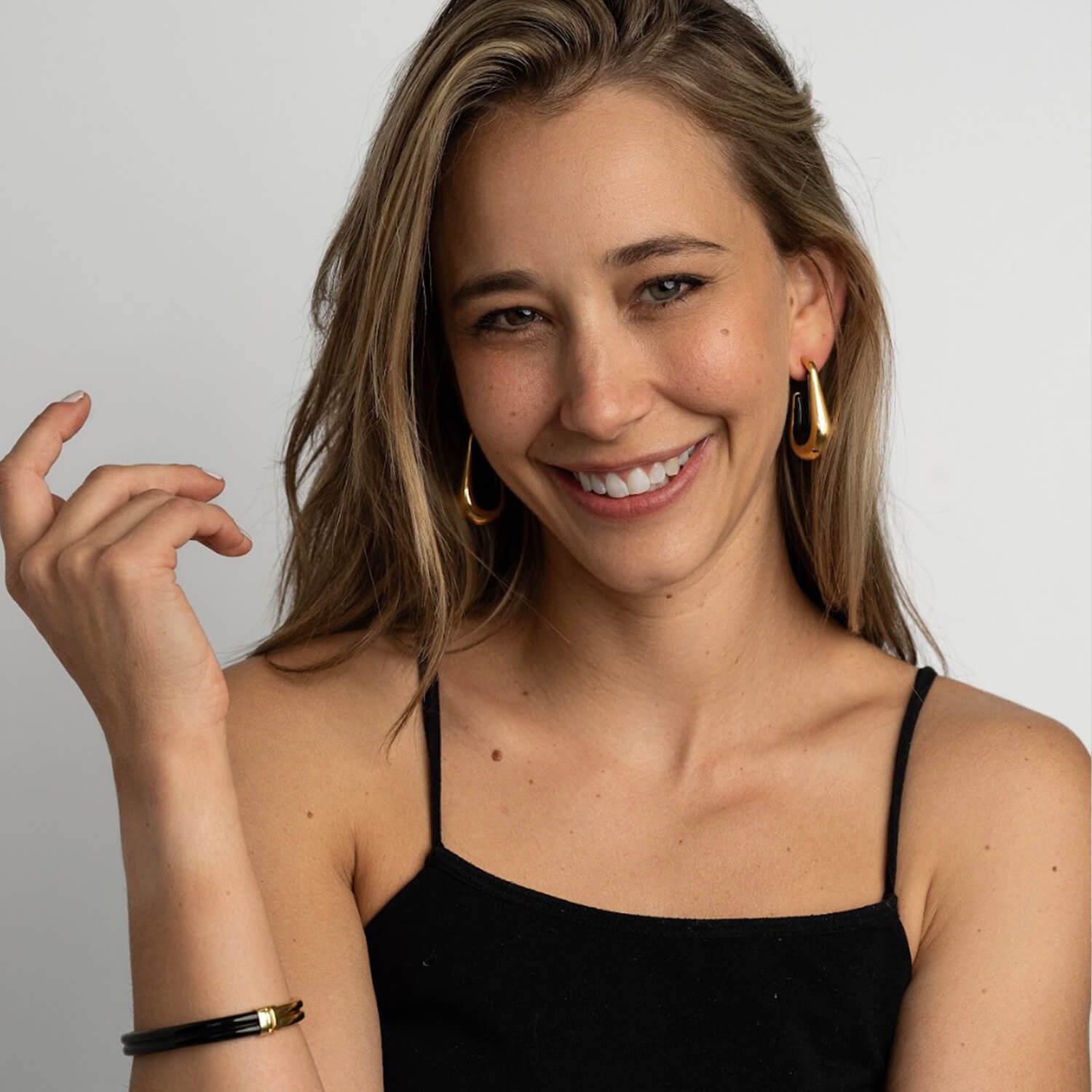 Woman wearing gold hoop earrings and a black top against a plain background