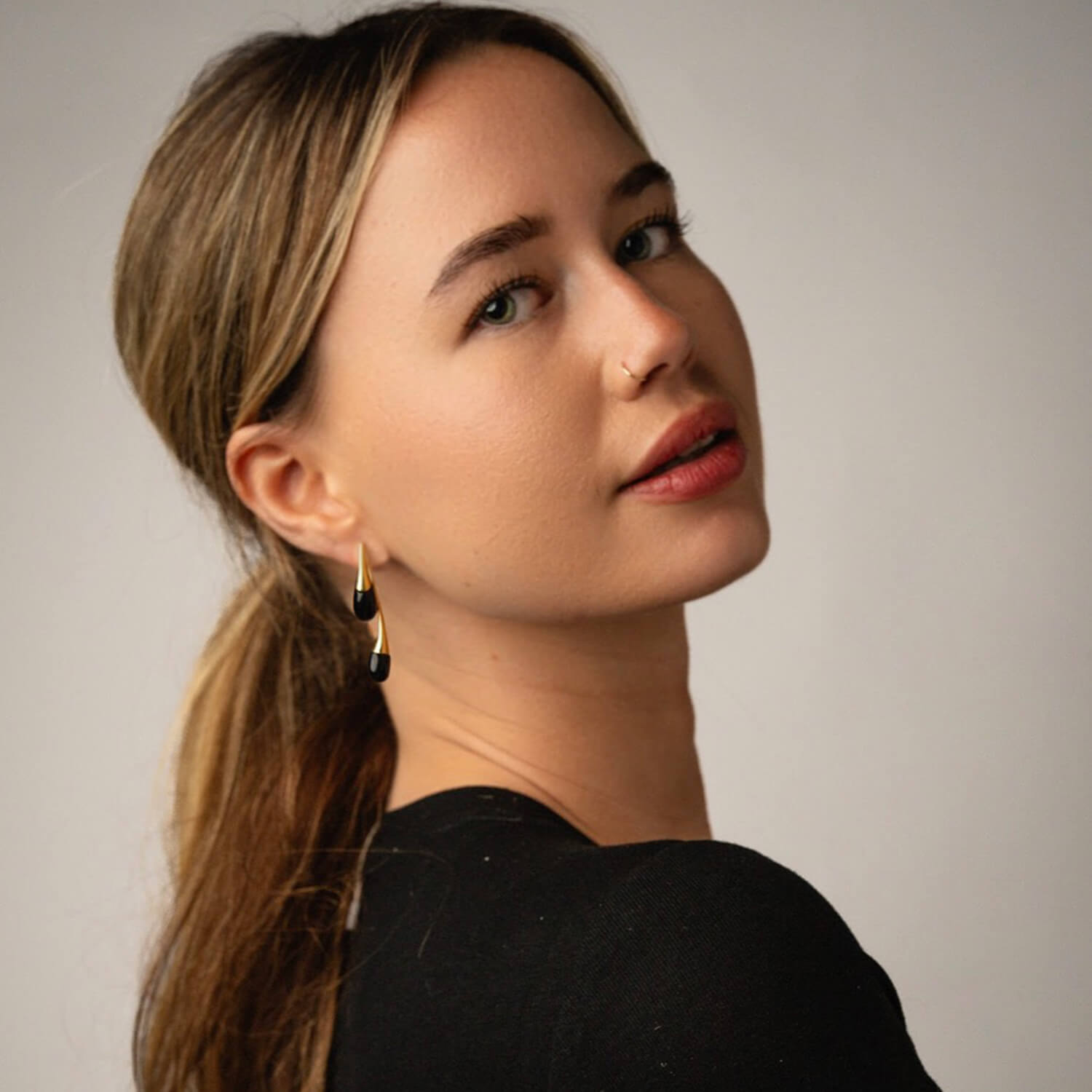 Woman wearing black earrings against a neutral background