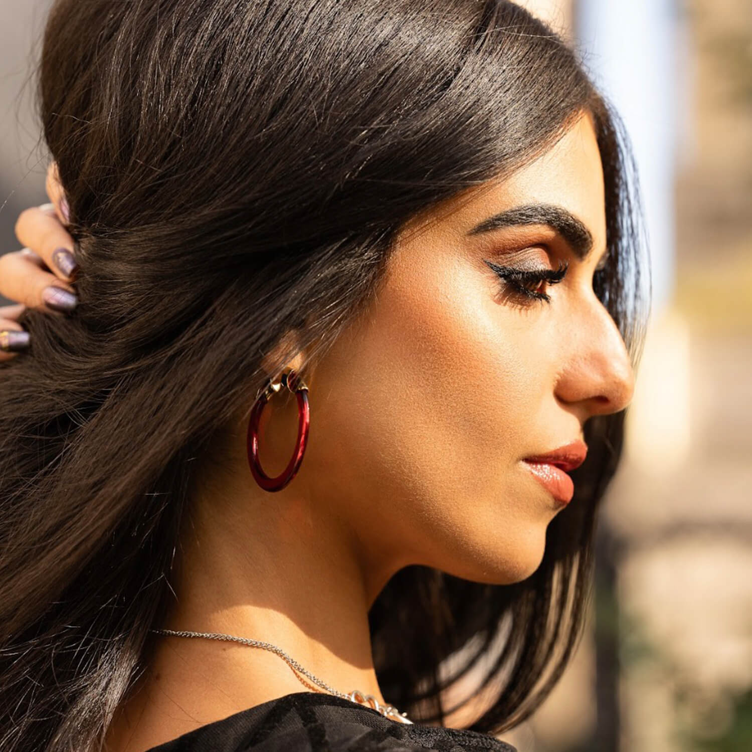 Woman with red hoop earrings and a blurred outdoor background