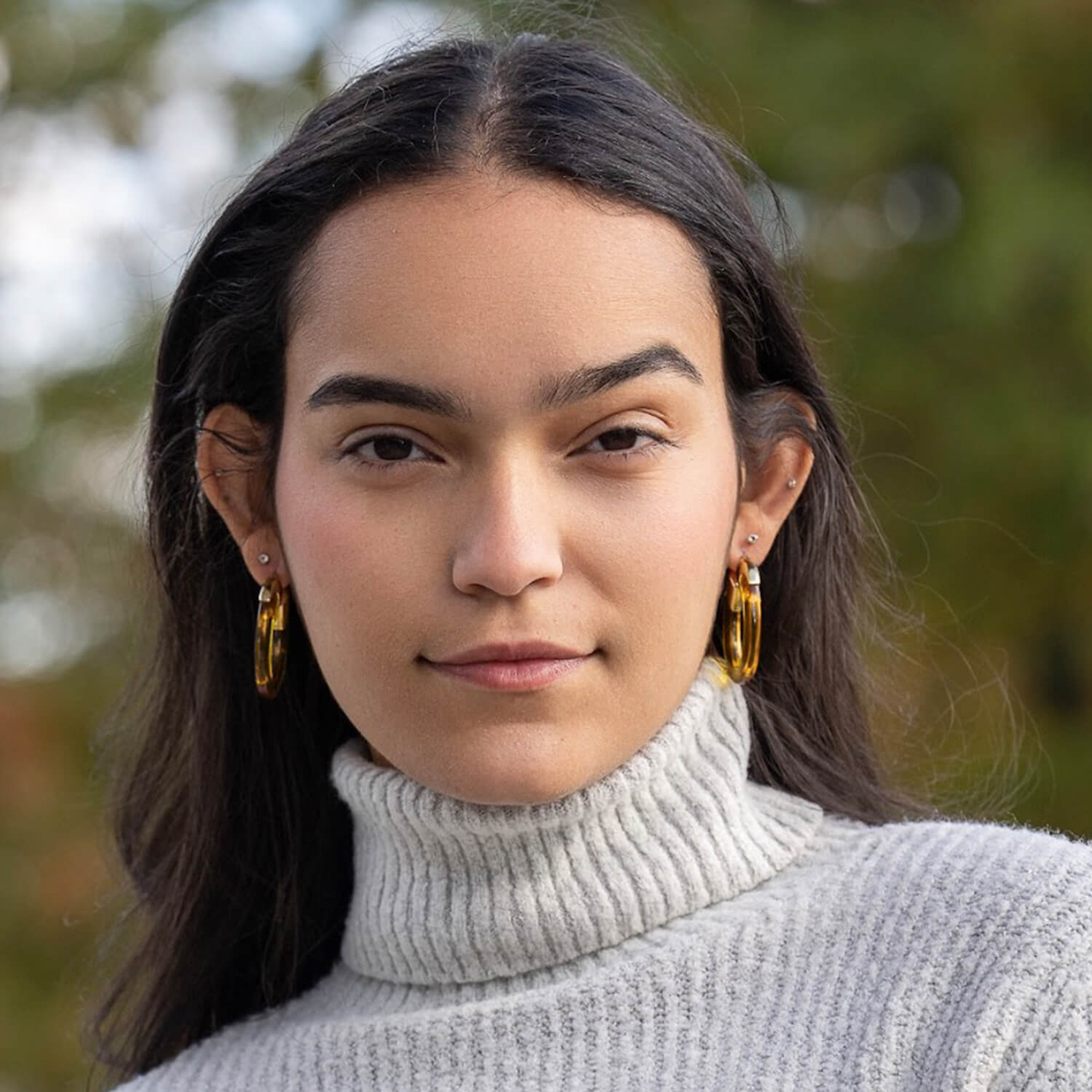 Woman wearing gold hoop earrings with a blurred natural background