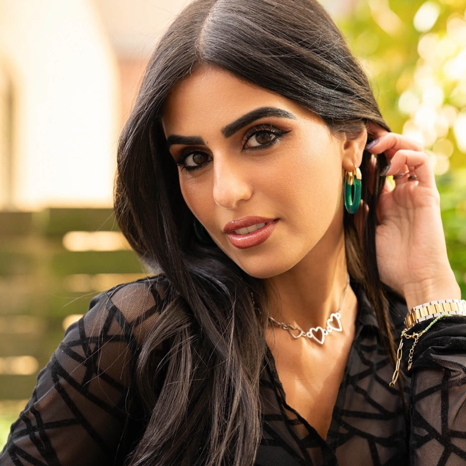 Woman adjusting her earrings with a blurred outdoor background