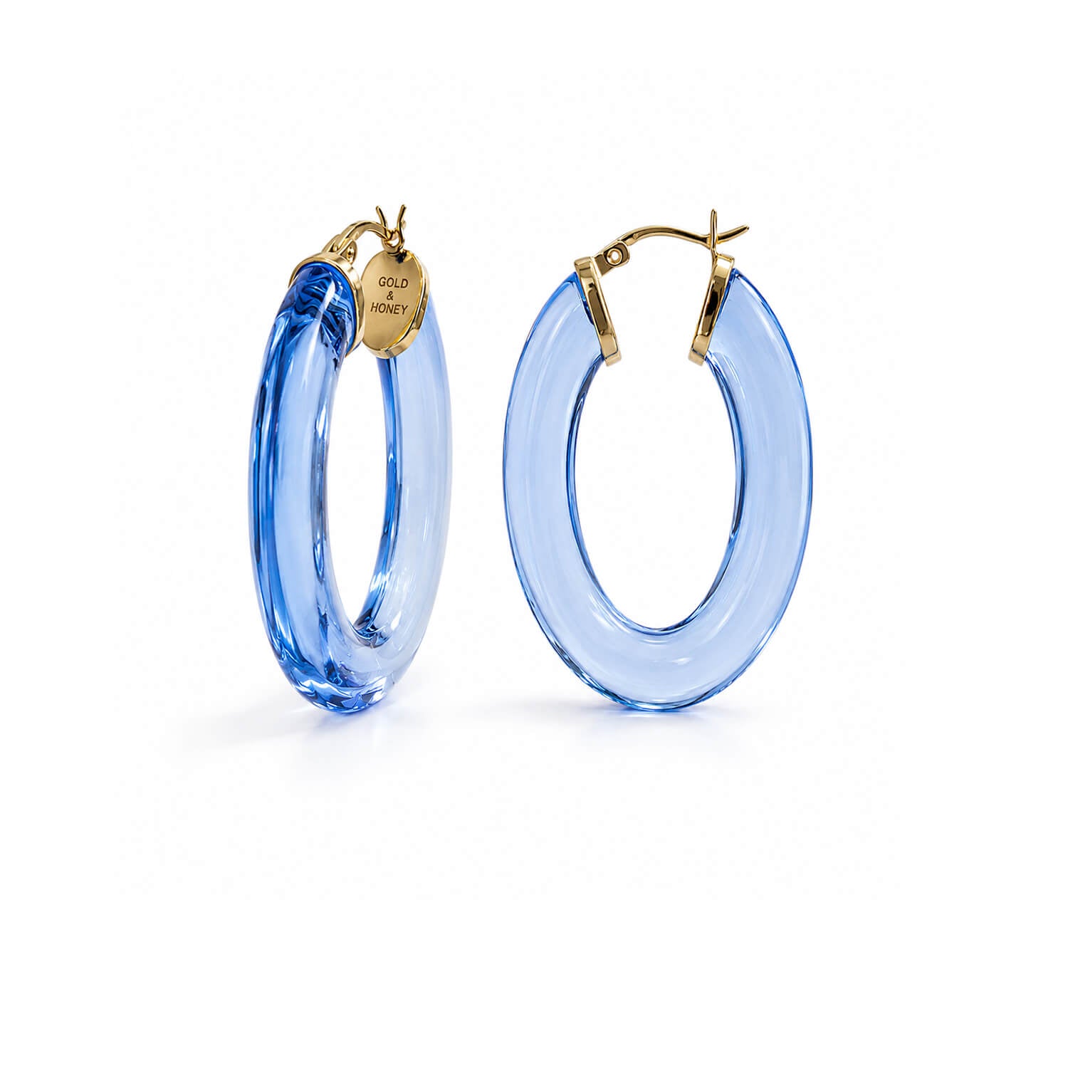 A pair of large, translucent light blue hoop earrings with gold-tone fishhook backings and a small round brand tag on one earring, shown against a plain white background.