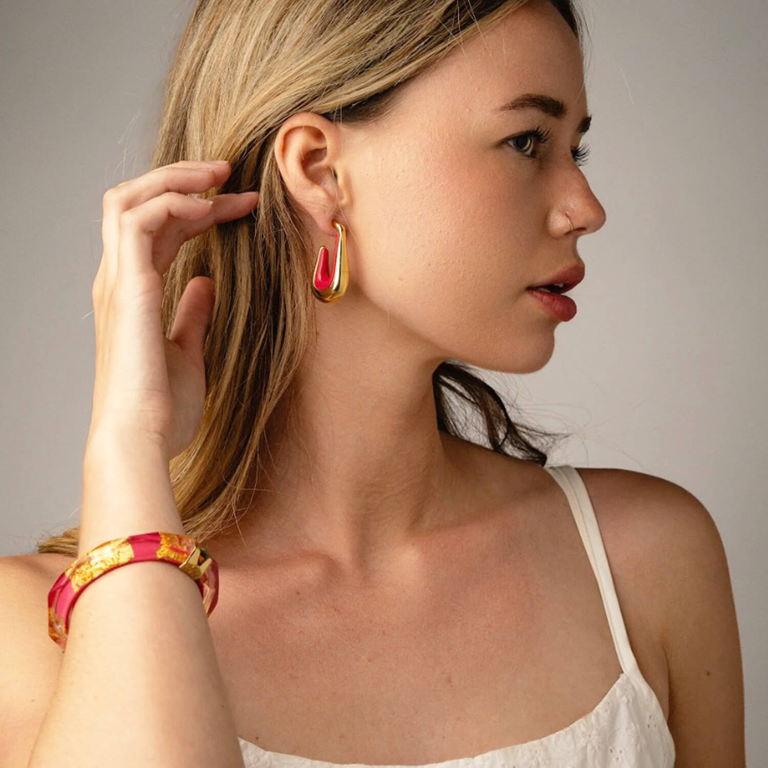Woman wearing colorful earrings and a bracelet against a neutral background