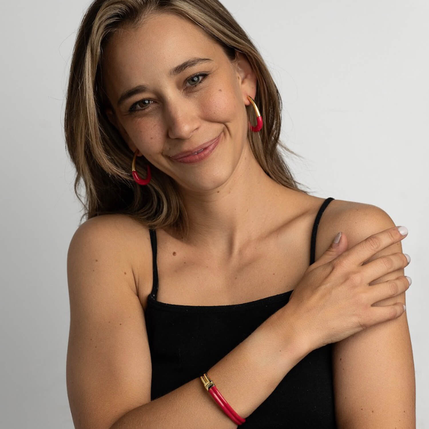Woman wearing a black top with pink earrings and bracelet on a plain background