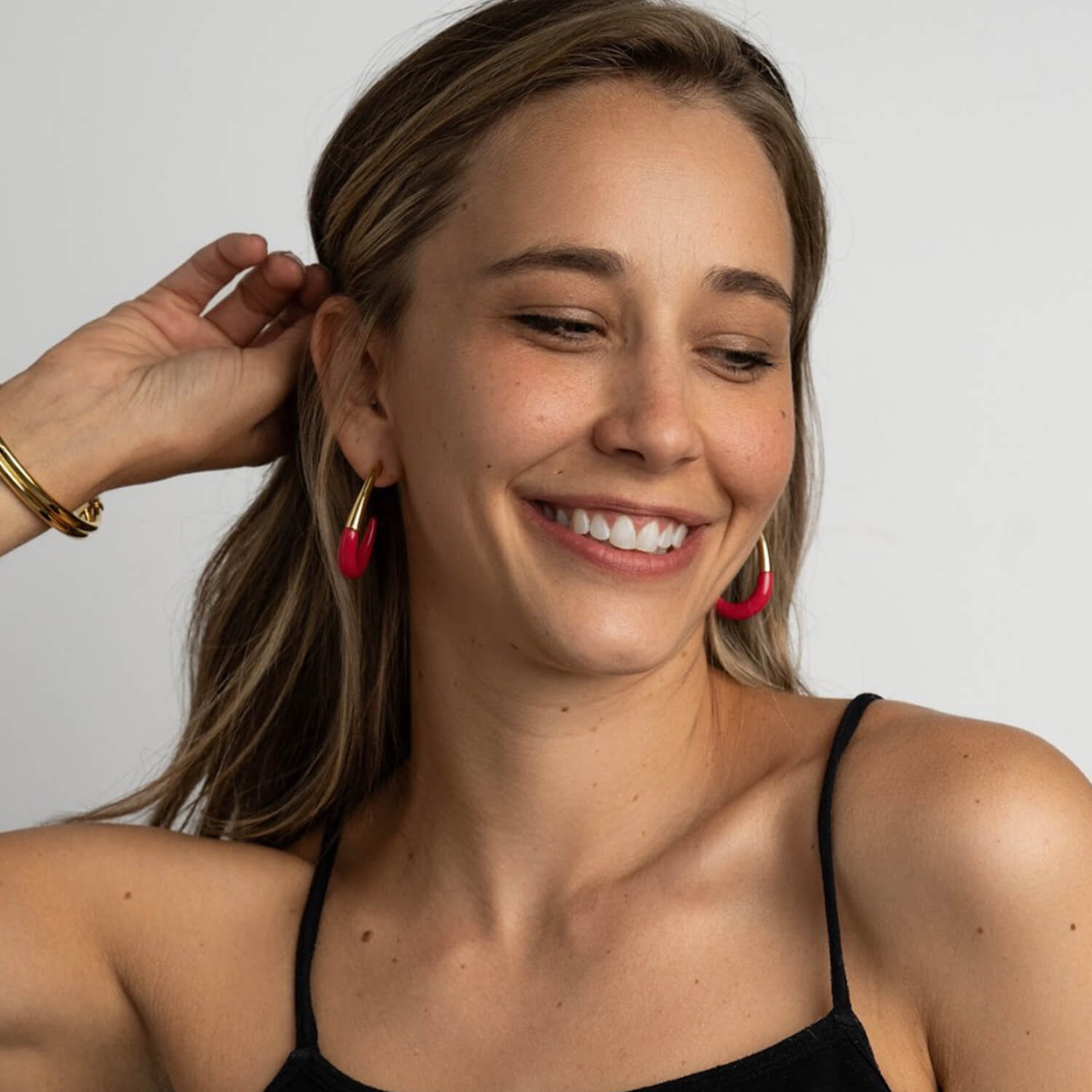 Woman wearing pink hoop earrings and a black top against a plain background