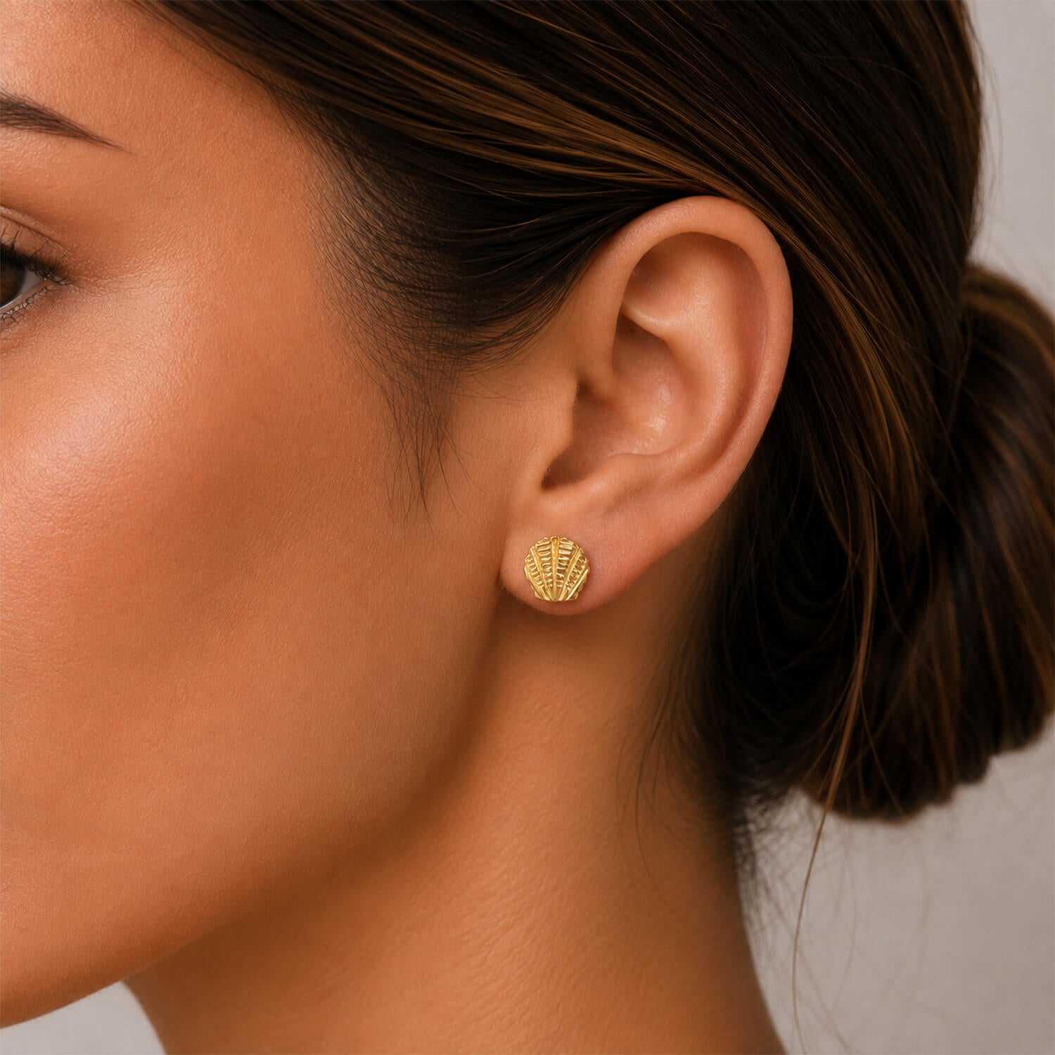Close-up of a person wearing gold earrings with a neutral background