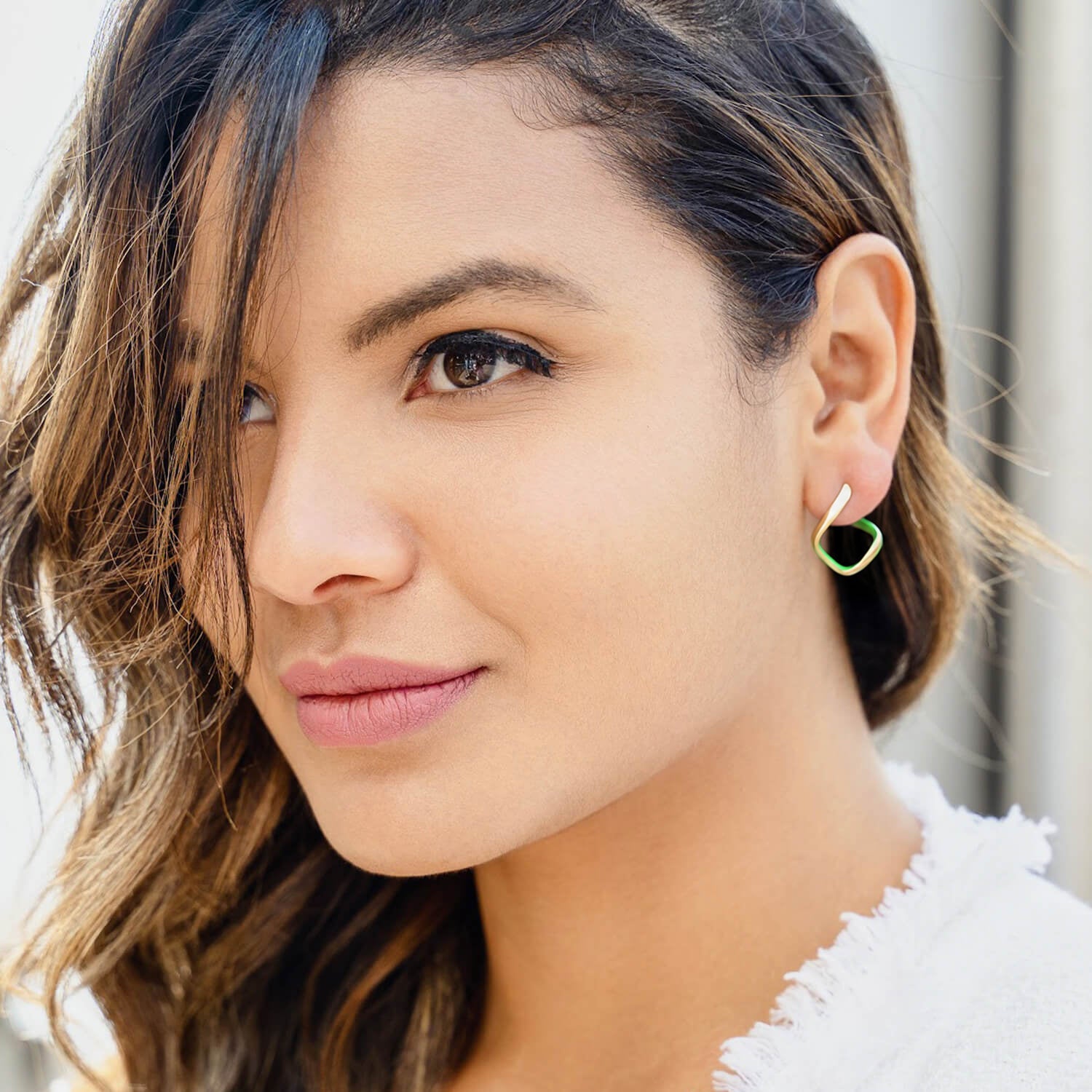 Close-up of a woman wearing a gold hoop earring with a red heart charm.