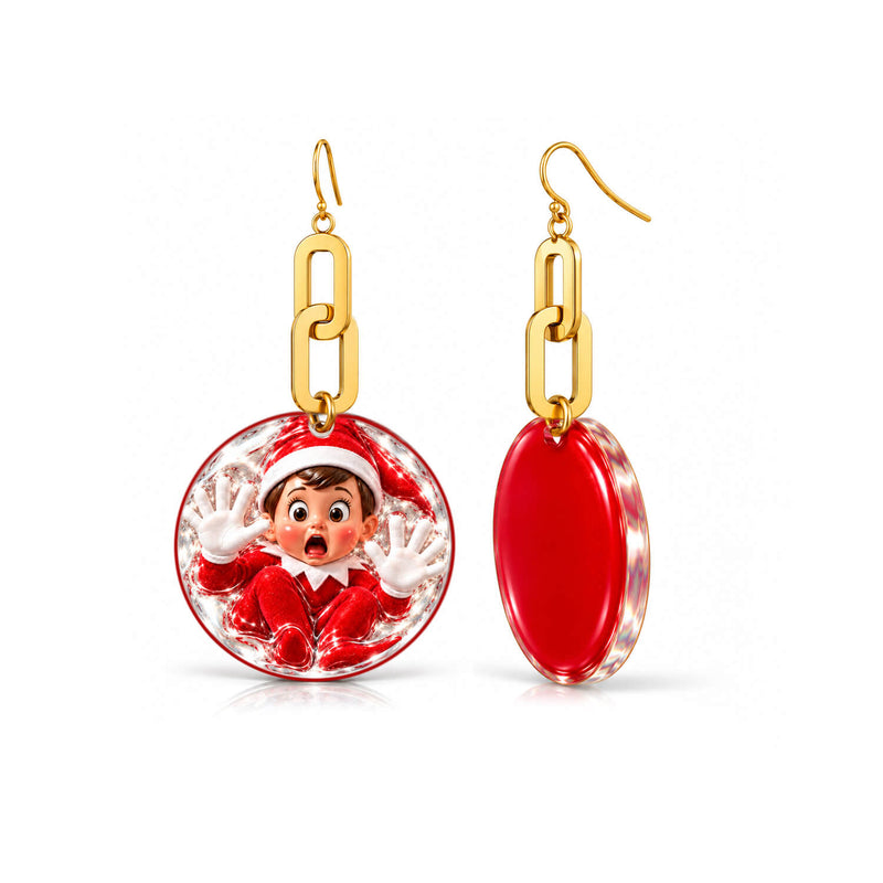 A pair of gold-tone dangle earrings on a white background. One earring is front-facing and shows a circular clear pendant with a cartoon elf in a red Santa outfit inside, suspended by gold chain links.