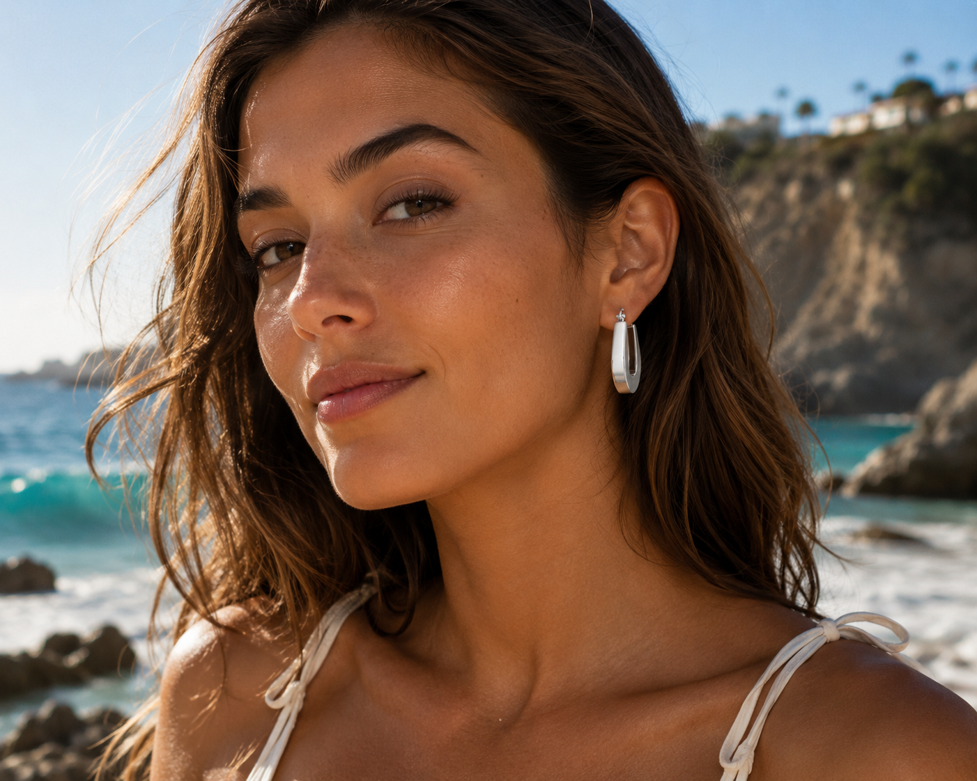 Woman with hoop earrings standing on a rocky beach with ocean and cliffs in the background