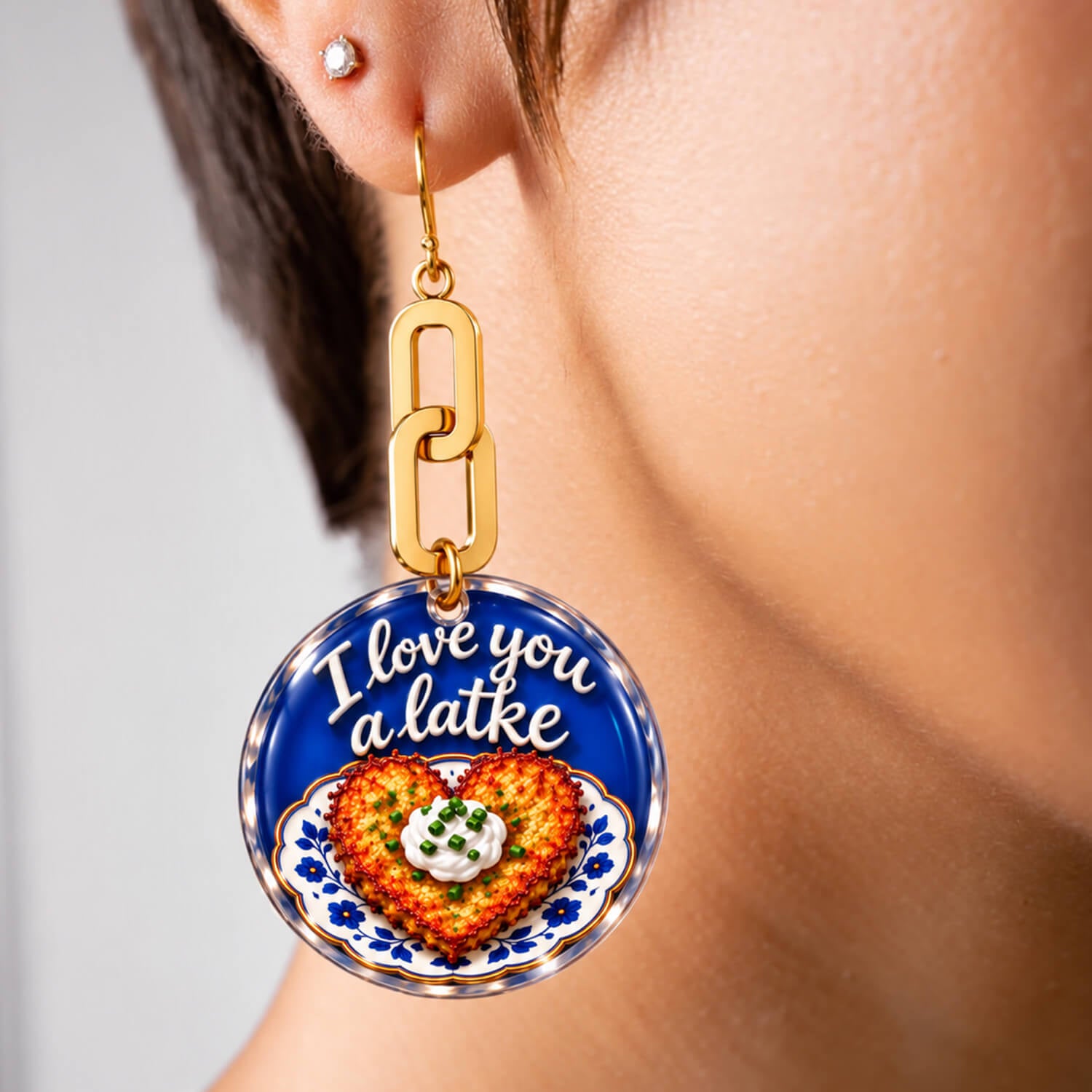 A pair of gold-tone dangle earrings on a white background. One round pendant shows a colorful food illustration with the text 'I love you a latte' on a blue background, and the other pendant is a textured gold oval.