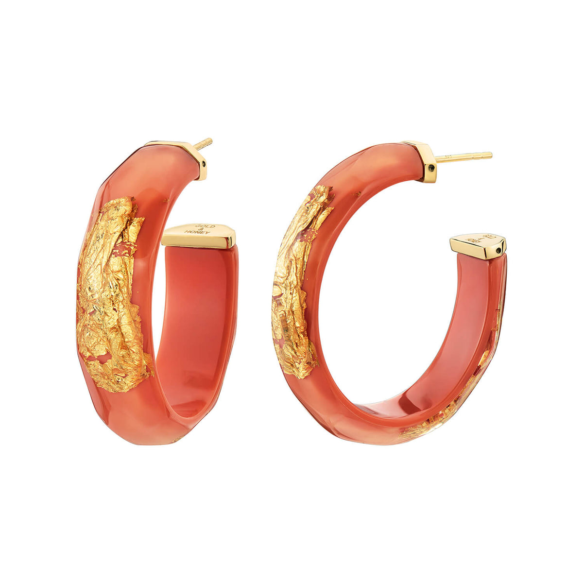 A pair of chunky hoop earrings with a translucent coral-red resin body and textured gold foil inlay, shown on a plain white background.