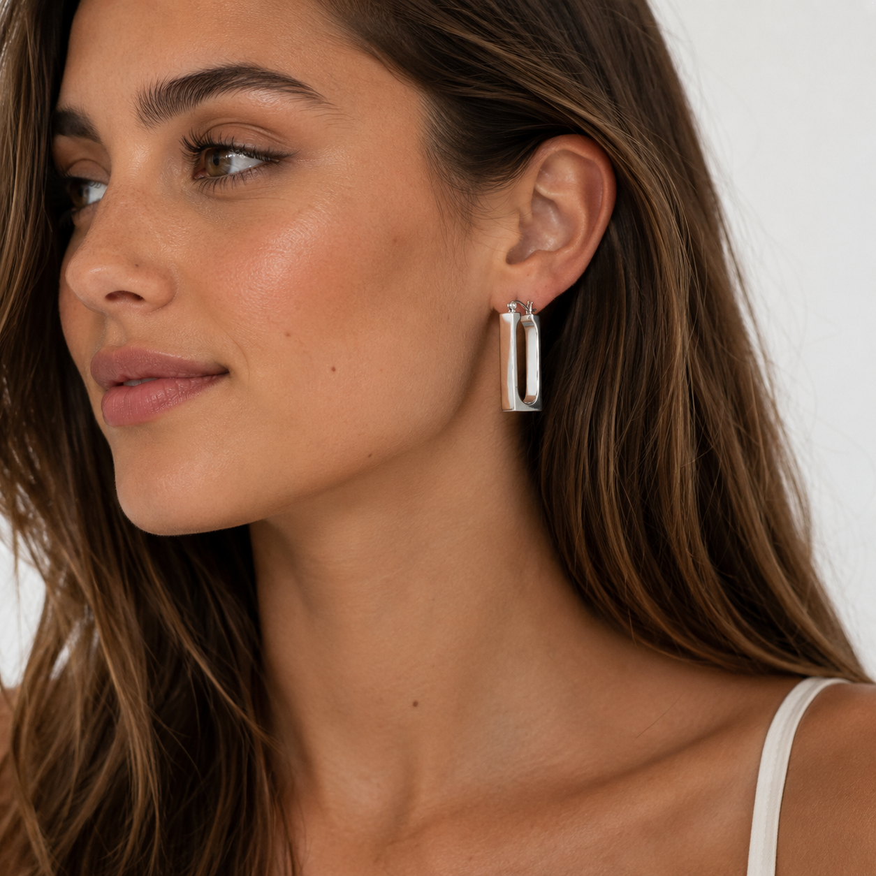 Close-up of a woman wearing silver hoop earrings with a neutral background