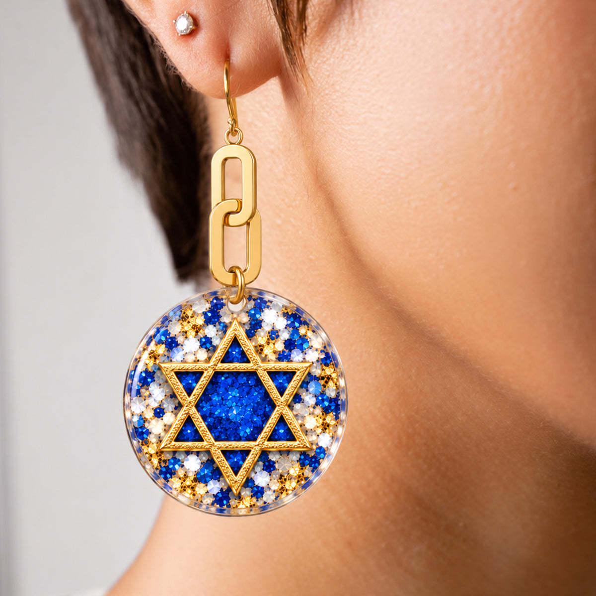 Close up of a model earring a drop earring wth a star of david and glitter print