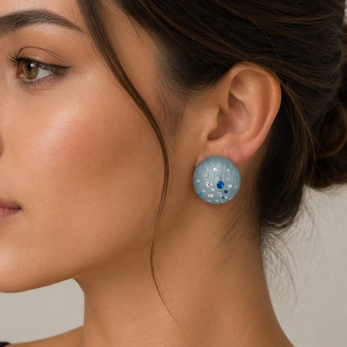 Close-up of a woman wearing blue earrings with a neutral background