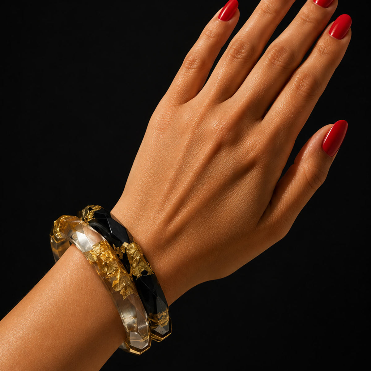 Hand wearing two bracelets with red nail polish on a black background