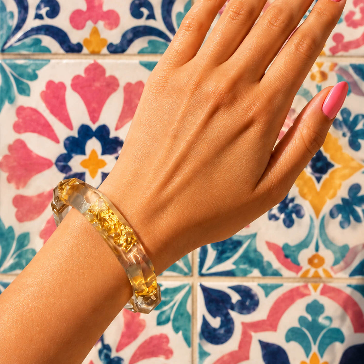 Hand wearing a clear bracelet with a colorful tiled background