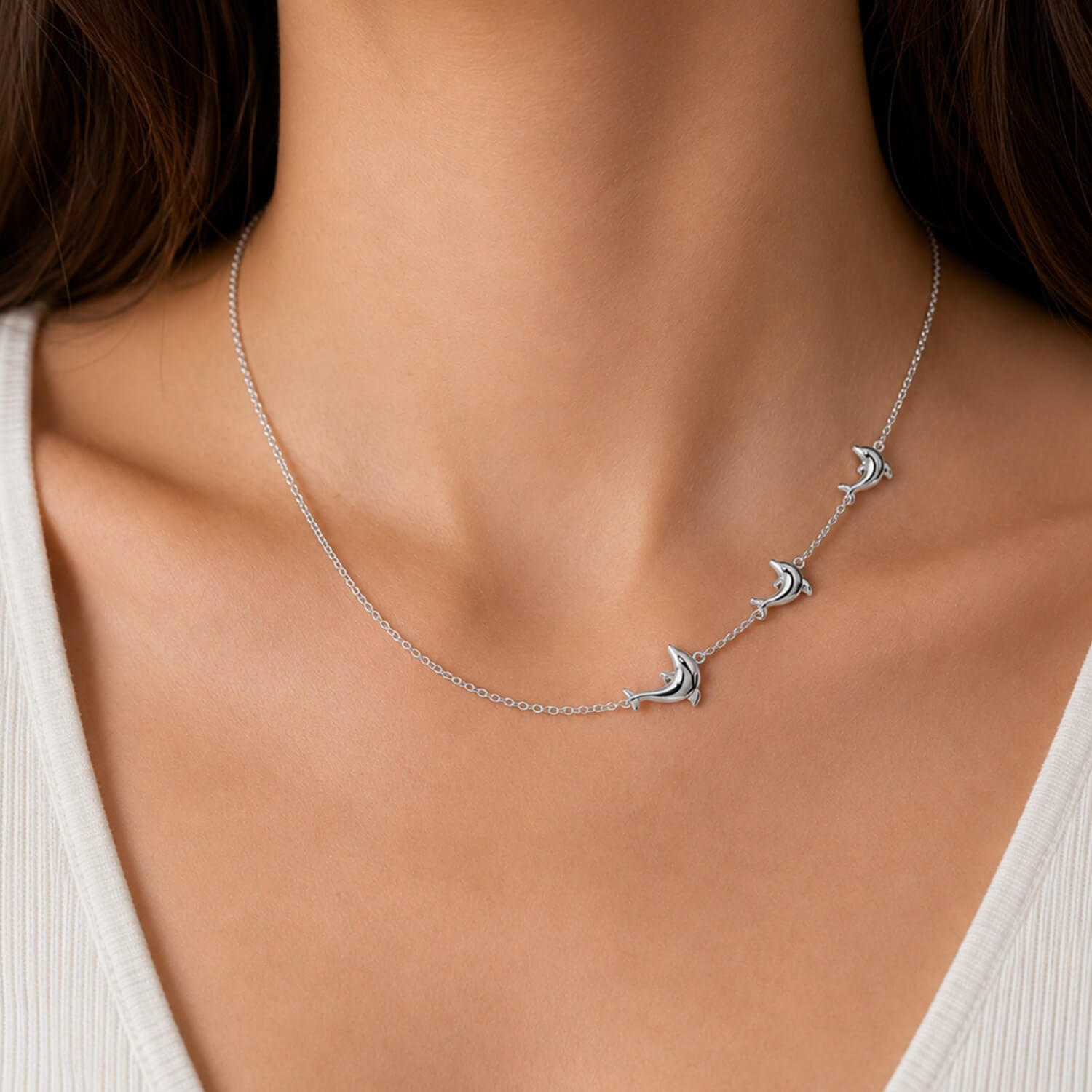 Silver necklace with dolphin charms on a person wearing a white top.