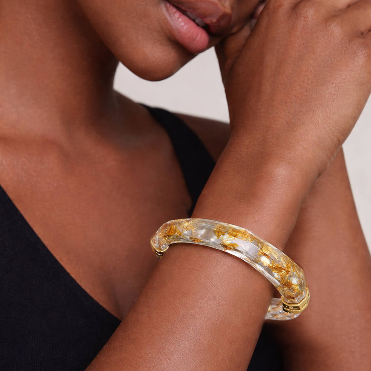 Close-up of a person wearing a gold and clear bracelet on a neutral background