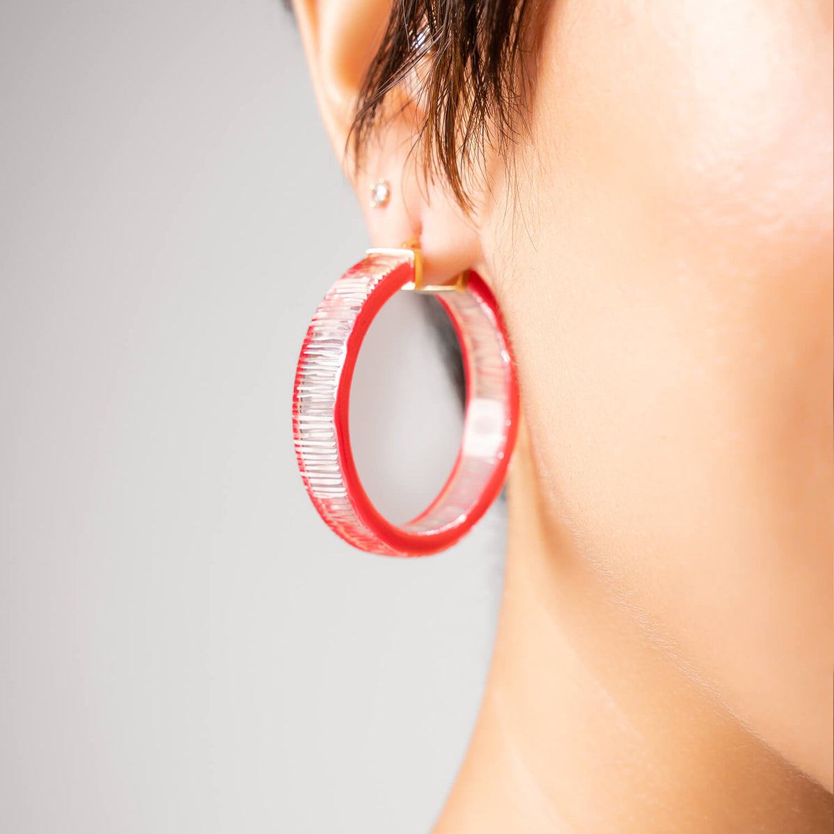 A close-up side view of a person's ear wearing a large textured pink hoop earring with a gold post 