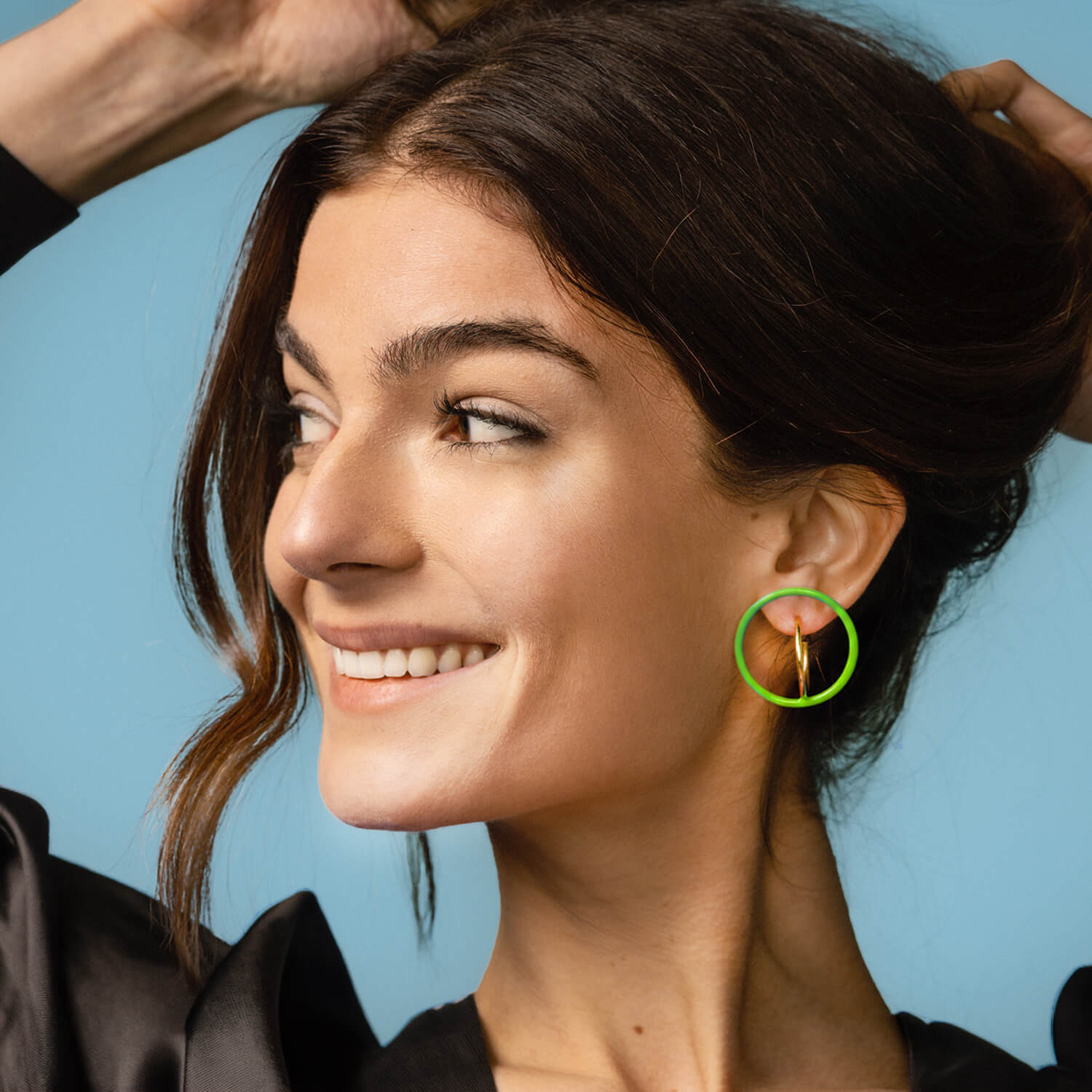 woman holding up her arms and wearing a  floating neon green hoop illusion with a gold hoop 