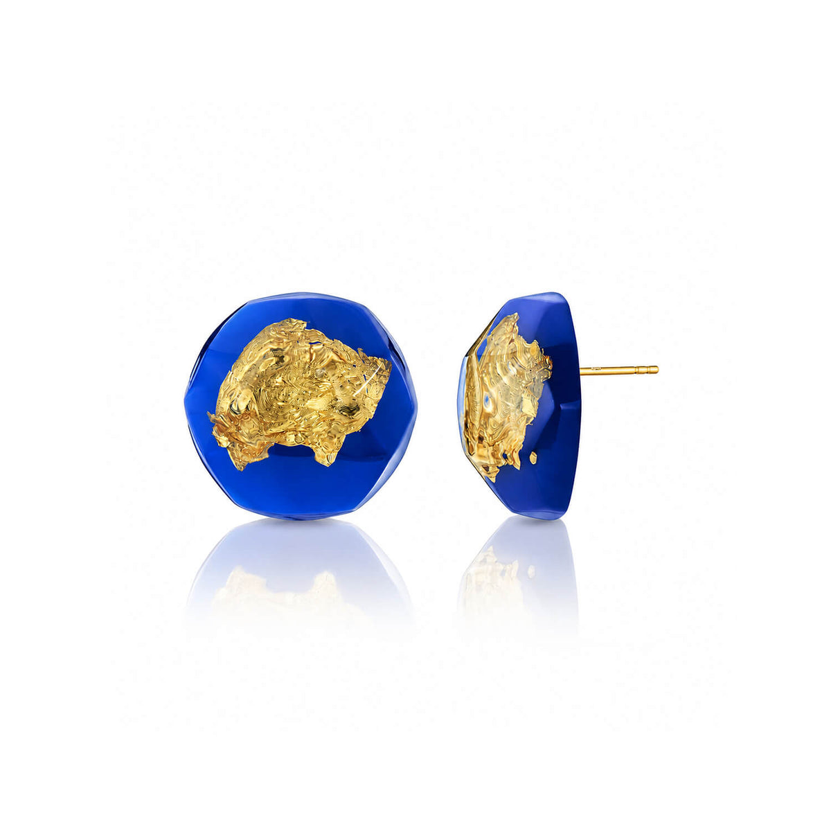 A pair of gold and cobalt blue stud earrings on a white reflective background. One earring is shown from the front, displaying a textured gold surface set within a faceted deep blue base, while the other is shown from the side, displaying the gold backing and post.