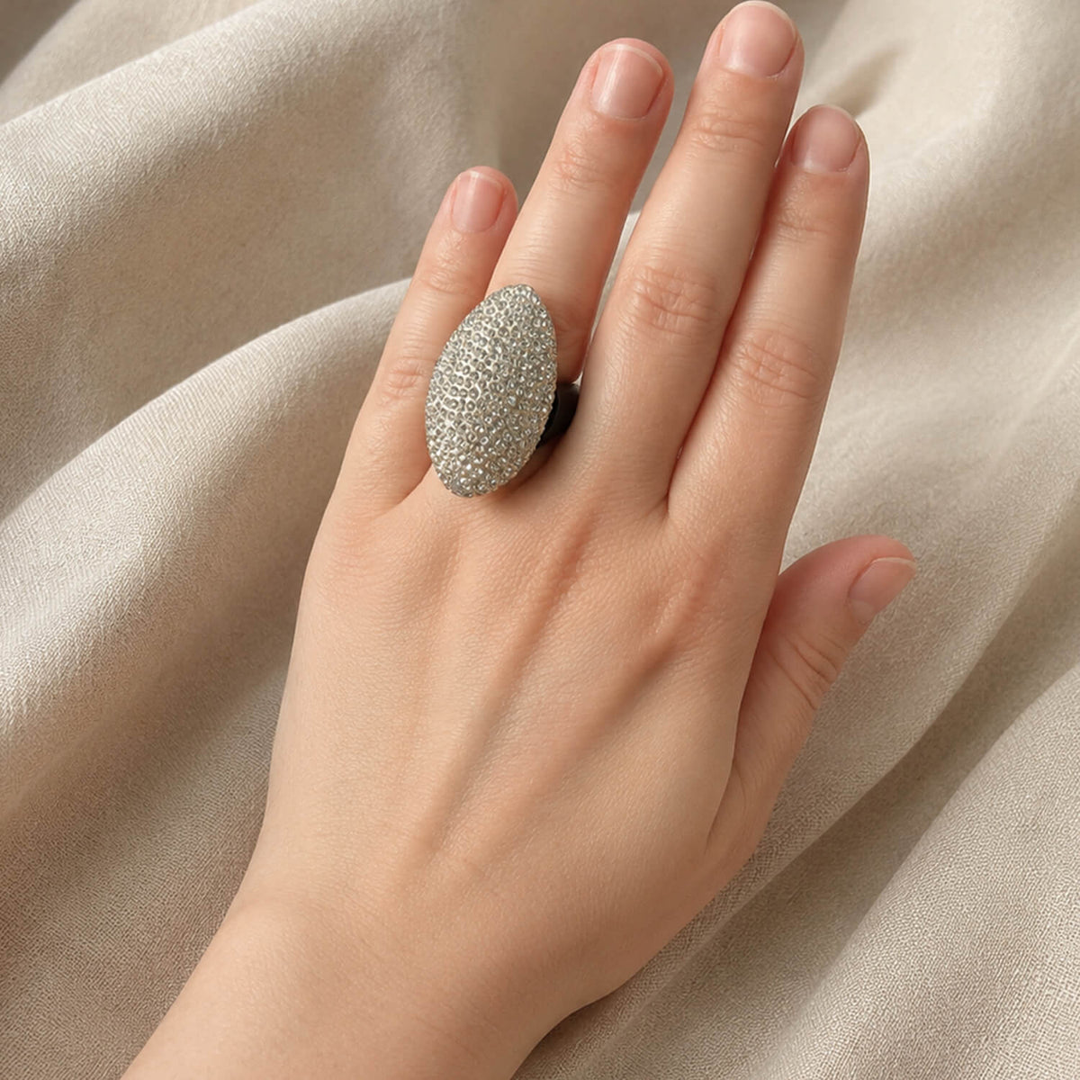 Hand wearing a Crystal ring on a beige fabric background