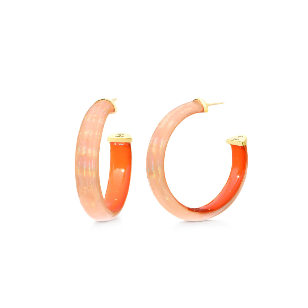 A pair of gold hoop earrings with a translucent peach-orange resin inlay, displayed against a solid white background.