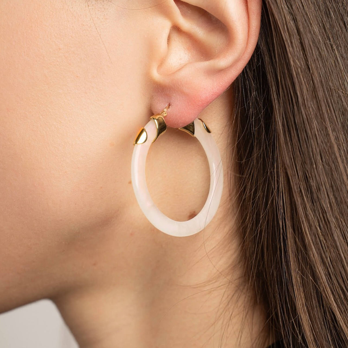 Close-up of a person wearing a gold hoop earring with a beige center.