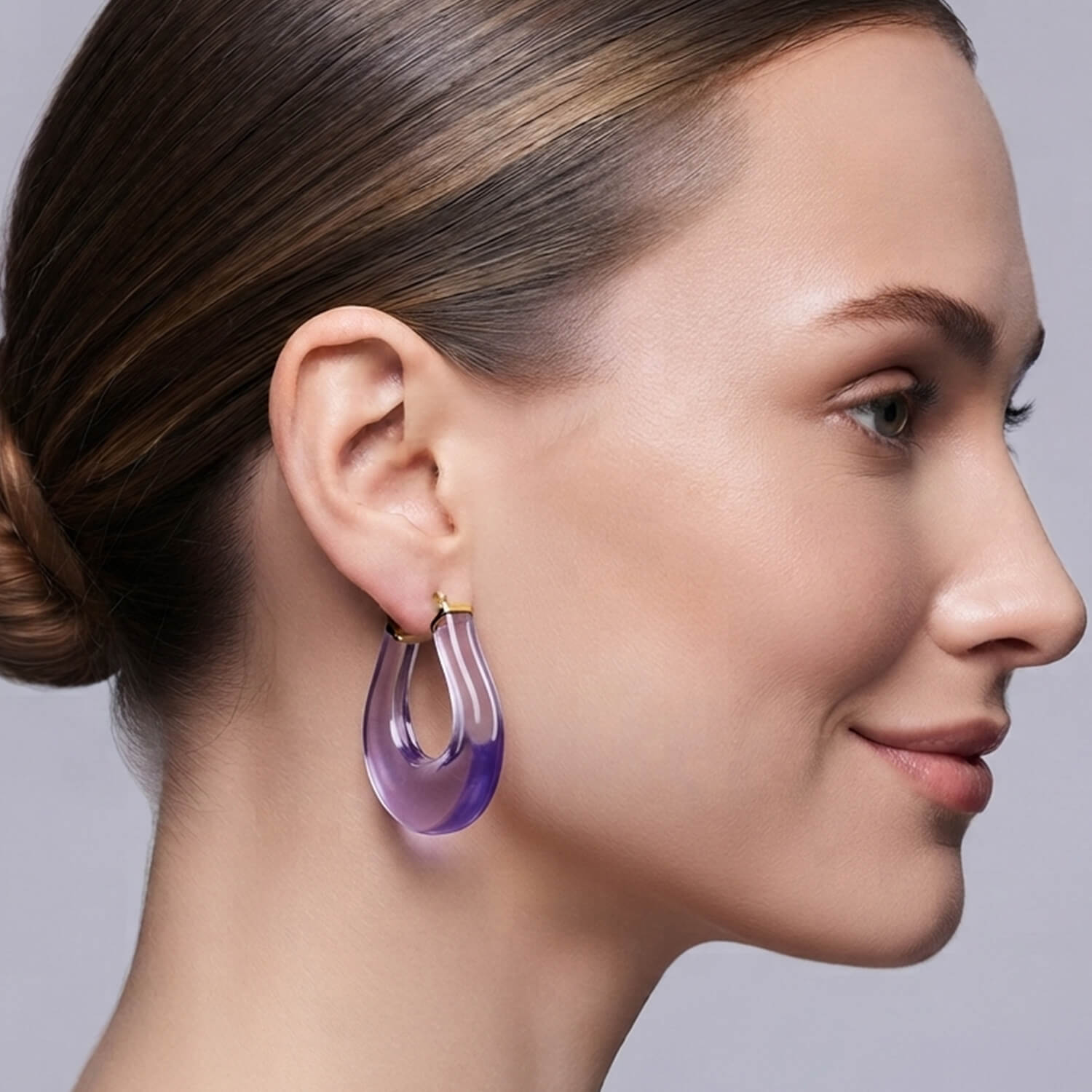 A pair of purple translucent hoop earrings with gold-tone posts, displayed on a clean white background.