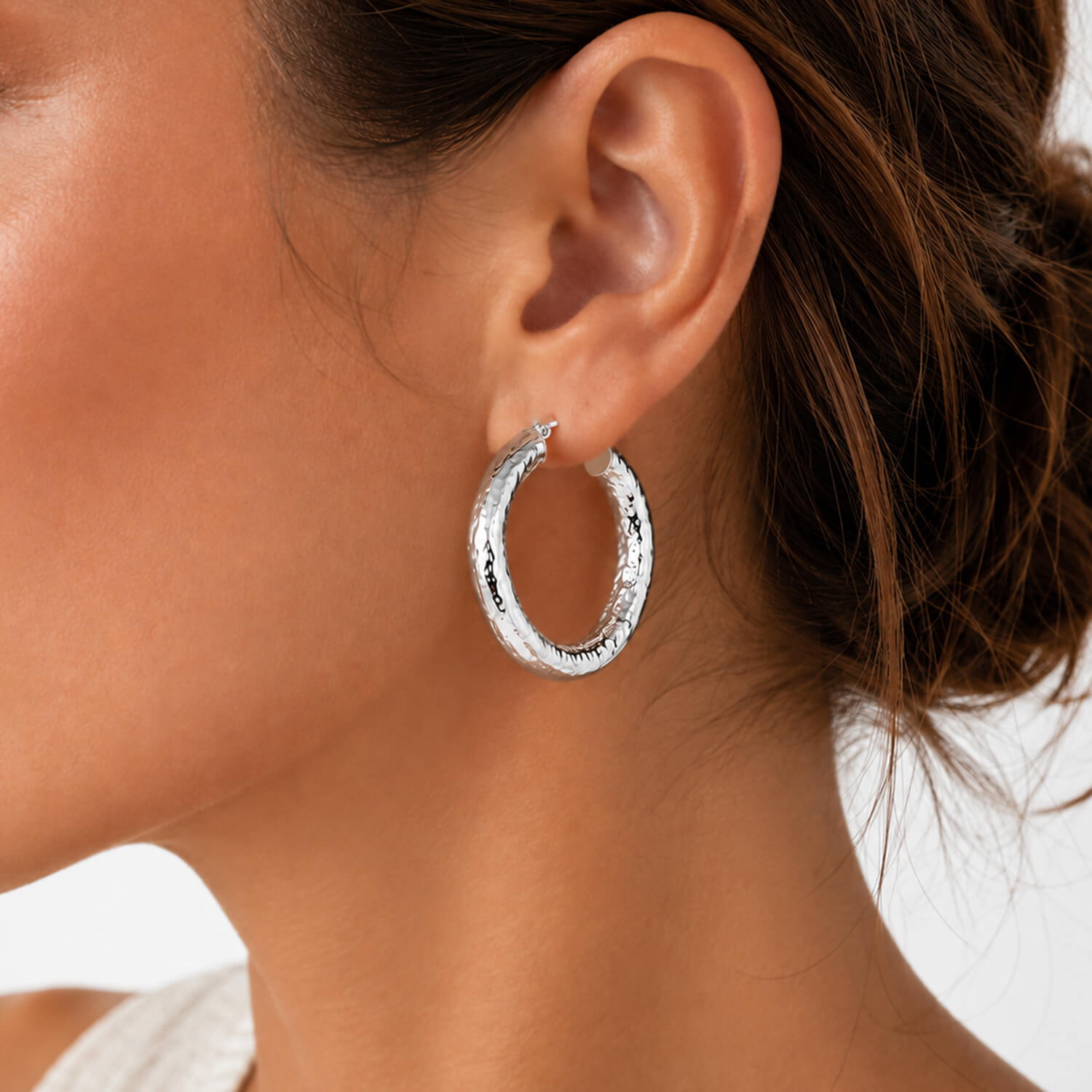 A pair of silver hoop earrings with a textured, hammered finish, shown from both a side profile and a front-facing view on a clean white background.