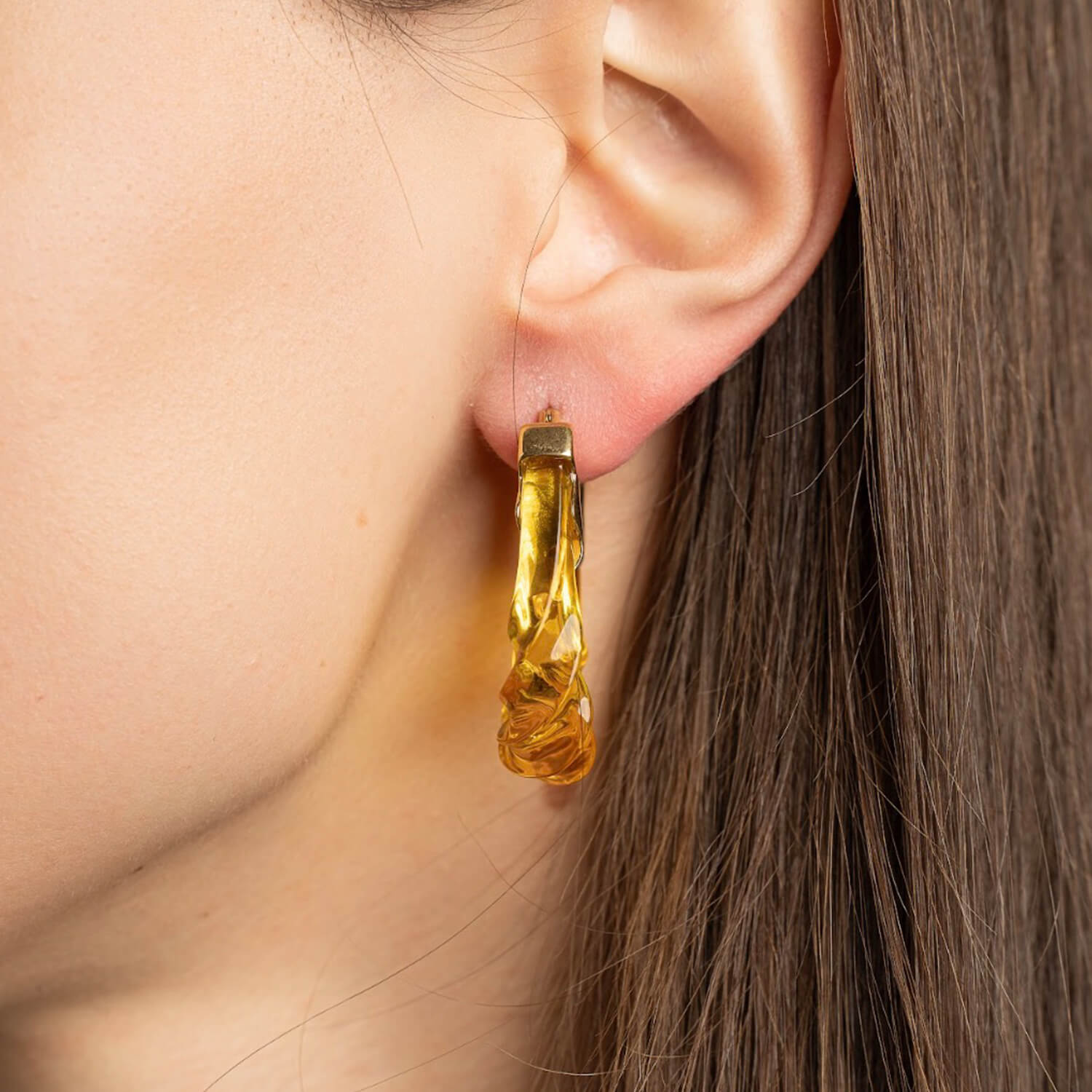 Close-up of a person wearing a gold hoop earring with a blurred background